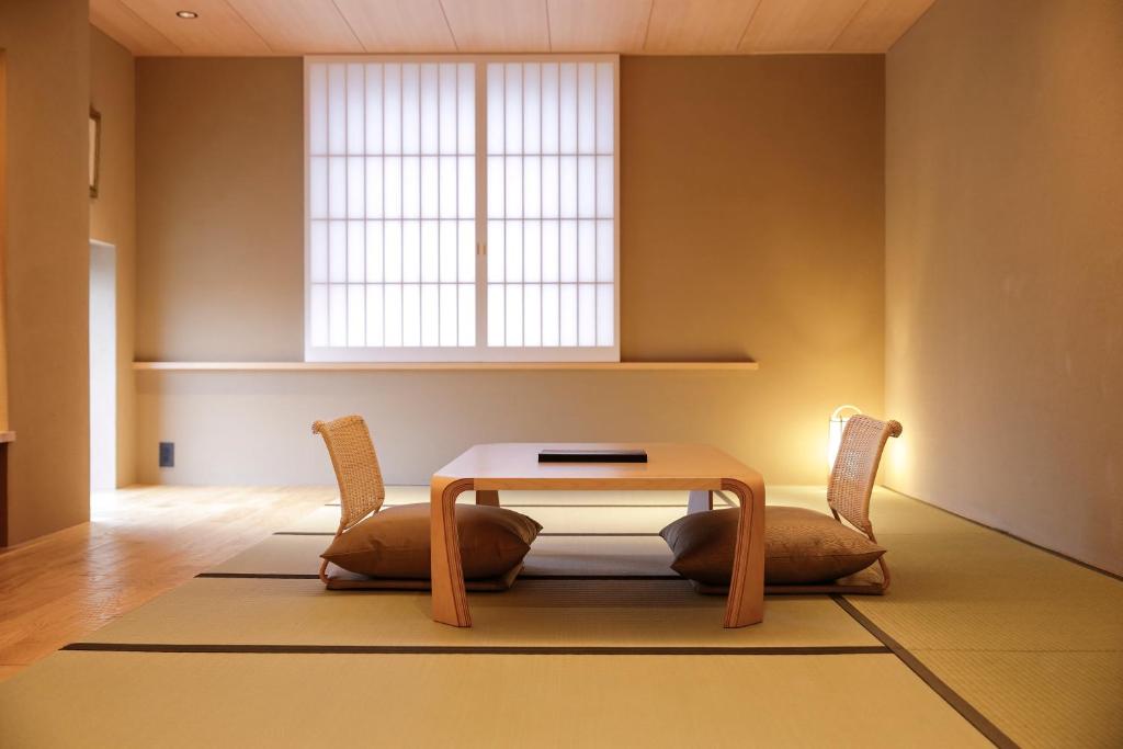 15 Unique Hotels in Tokyo: Coolest hotels 44 A minimalist Japanese-style room at one of the unique hotels in Tokyo, featuring tatami mats, a low wooden table, two floor seats with cushions, and soft natural light filtering through shoji paper doors in the background.