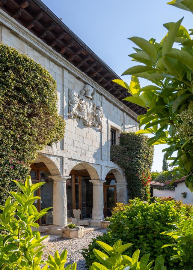 This historic stone building, resembling the charming hotels in Cantabria, features arched windows and doorways, lush leafy plants, and climbing greenery under a clear blue sky. A decorative crest is proudly displayed above the entrance.