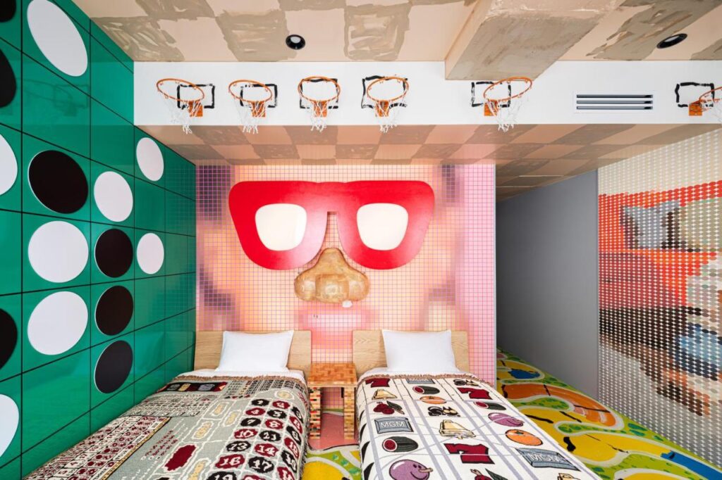 15 Unique Hotels in Tokyo: Coolest hotels 32 A colorful bedroom at one of the unique hotels in Tokyo, featuring two single beds with playful bedding, a mural of a face with red glasses, green and black circles on the wall, and mini basketball hoops above the beds.