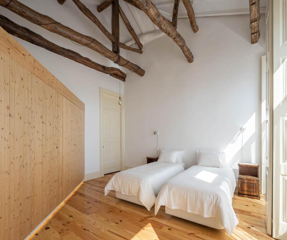 Top 12 Boutique Hotels in Porto, Portugal 40 Minimalist bedroom with two single beds, white bedding, wooden floor, rustic ceiling beams, built-in wardrobe, and sunlight streaming through tall windows—a serene space inspired by boutique hotels in Porto.