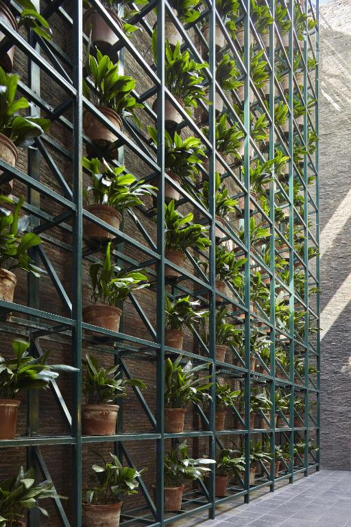 13 Unique Hotels in Barcelona, Spain 32 A tall, metal grid structure holds numerous potted green plants arranged in neat rows against a brick wall, with sunlight streaming in from the right side—a stylish feature often seen in unique hotels in Barcelona.