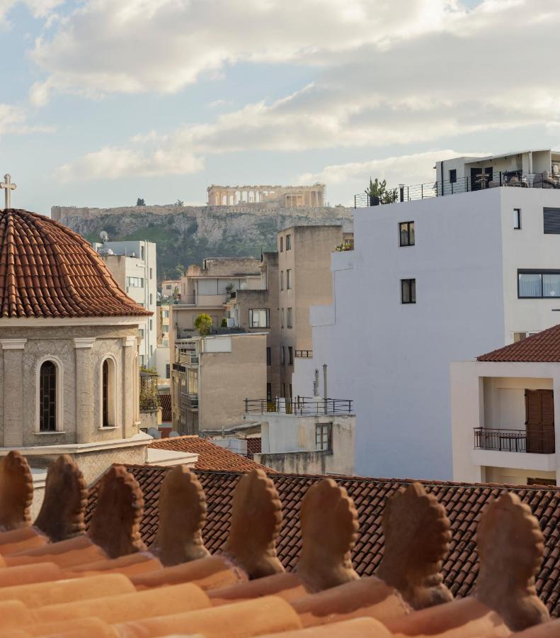 Rooftops and buildings in Athens with a domed church in the foreground; the Acropolis and Parthenon rise in the distance—an inspiring sight often enjoyed from the best boutique hotels in Athens under a partly cloudy sky.
