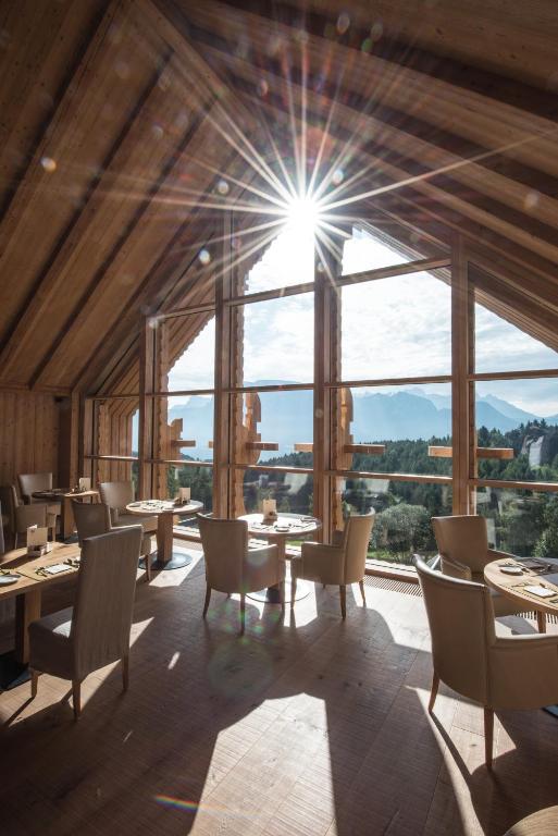 A sunlit restaurant with wooden interiors and large windows offers scenic mountain views. Elegant tables and chairs are arranged for dining, making it a standout feature among the best hotels in the Dolomites.