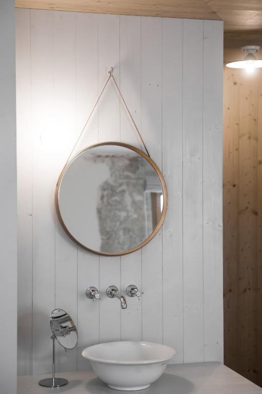 A round mirror hangs above a white sink and chrome faucet on a slatted wooden wall, echoing the elegant bathroom designs found in the best hotels in the Dolomites.