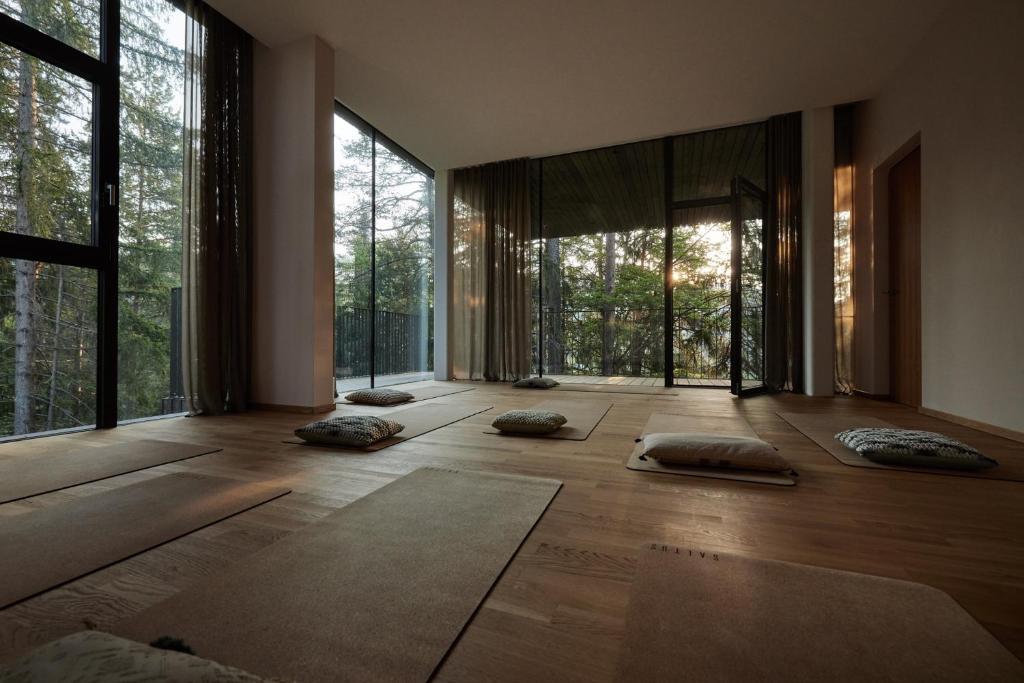 A serene yoga studio with large windows, wooden floors, and cozy mats echoes the peaceful ambiance found in the best hotels in the Dolomites, as sunlight filters through tall trees to create a natural retreat.