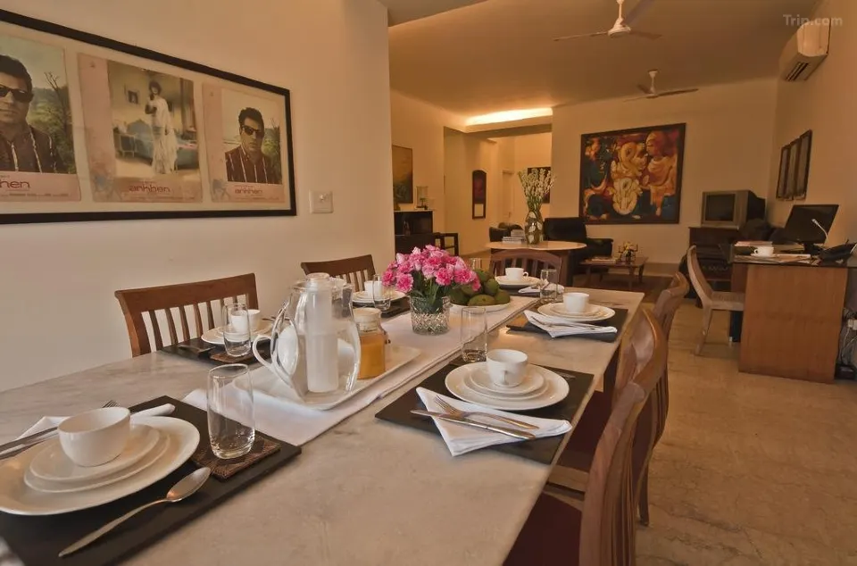 A dining room with a marble table set for four, featuring white dishes and a centerpiece of pink flowers—reminiscent of the elegant interiors found in boutique hotels in New Delhi. The cozy space includes wall art, a desk, and warm lighting.