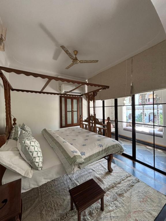 9 Iconic Heritage Hotels in Udaipur 17 A bright bedroom in one of the heritage hotels in Udaipur, featuring a wooden four-poster bed, patterned pillows, a ceiling fan, and large glass doors opening to a sunlit seating area outside.