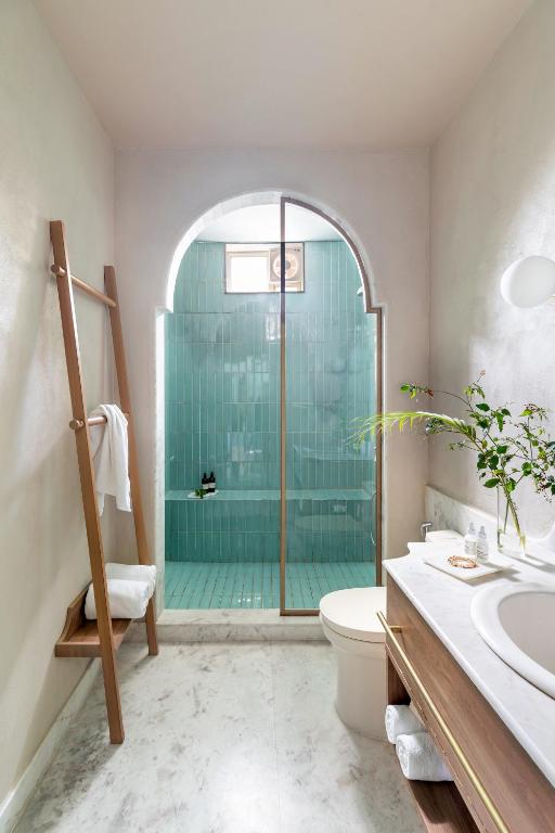 9 Iconic Heritage Hotels in Udaipur 8 Modern bathroom with a marble floor, wooden towel rack, vanity with a round sink, and a walk-in shower featuring teal tiles and an arched glass door—evoking the elegance found in heritage hotels in Udaipur. A small plant sits on the vanity.