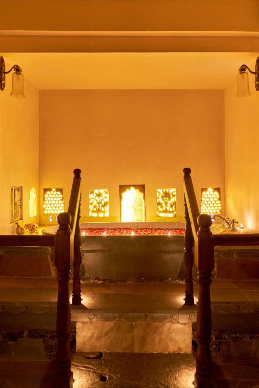 9 Iconic Heritage Hotels in Udaipur 21 A warmly lit indoor spa area in one of the finest heritage hotels in Udaipur, with a sunken tub, rose petals floating on the water, glowing decorative lights on the walls, and wooden railings leading down to the tub.