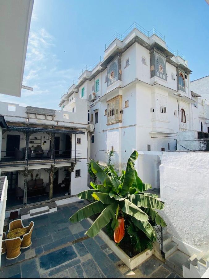 9 Iconic Heritage Hotels in Udaipur 4 A bright courtyard with a banana plant in the center, surrounded by white-washed buildings and traditional balconies, evokes the charm of heritage hotels in Udaipur. Outdoor seating rests in the corner beneath a clear blue sky.