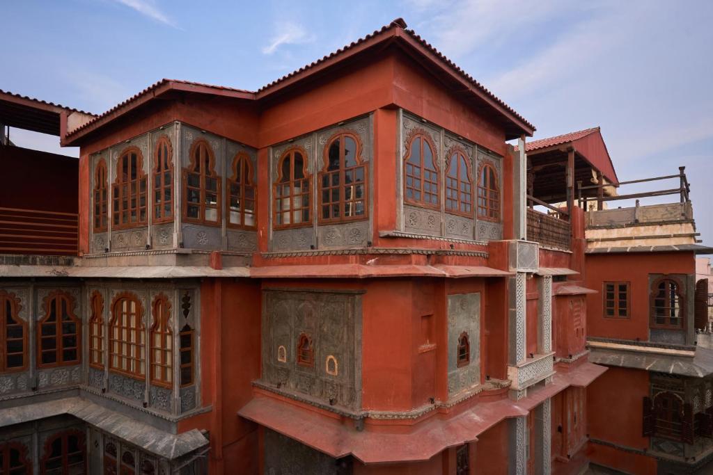 9 Iconic Heritage Hotels in Udaipur 20 A traditional building with red walls, arched wooden windows, and intricate grey stonework, this stunning example of heritage hotels in Udaipur features multiple levels and overhanging sections under a blue sky.