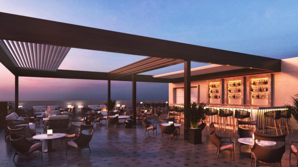 A modern rooftop bar at sunset with stylish seating, tables, and a well-lit bar area—a signature feature of boutique hotels in New Delhi. The open-air space with a pergola offers scenic views and a relaxed, elegant atmosphere.