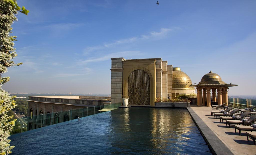 A rooftop infinity pool at one of the finest boutique hotels in New Delhi overlooks the city skyline, bordered by ornate golden domes and architectural arches. Lounge chairs line the poolside under a clear blue sky.
