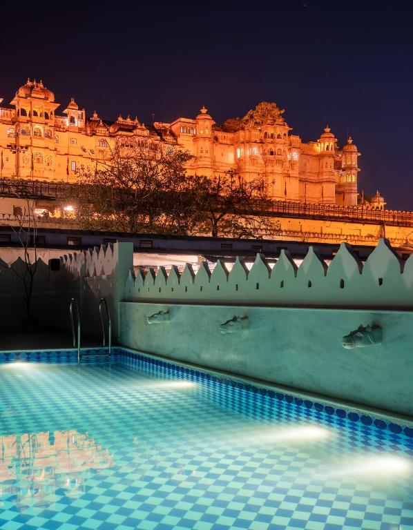 9 Iconic Heritage Hotels in Udaipur 10 A swimming pool with blue and white tiles is seen at night, set against the illuminated architecture of heritage hotels in Udaipur. The palaces' reflection shimmers in the tranquil water beneath a dark sky.