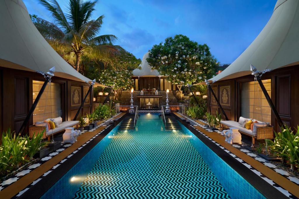 9 Iconic Heritage Hotels in Udaipur 28 Luxury outdoor pool surrounded by elegant tents, lush greenery, lounge chairs, and decorative lighting in a tropical garden setting at dusk—reminiscent of the ambiance found at heritage hotels in Udaipur.