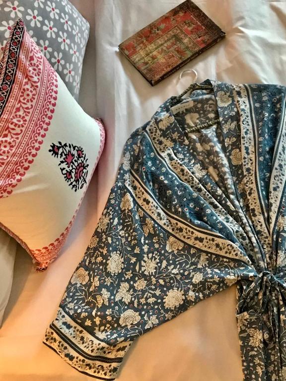 A blue and white floral robe is laid out on a bed next to a decorative pink and white pillow and a closed, patterned notebook, evoking the inviting ambiance of boutique hotels in New Delhi.