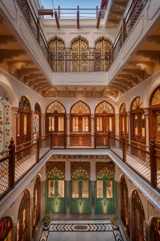 An ornate, multi-level atrium inspired by boutique hotels in New Delhi, with arched wooden doorways, decorative railings, stained glass windows, and intricate architectural details, beautifully illuminated by natural light from a skylight above.