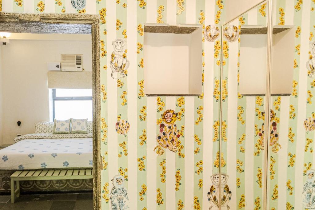 9 Iconic Heritage Hotels in Udaipur 15 A bedroom inspired by heritage hotels in Udaipur, with pastel green and white striped wallpaper featuring playful animal illustrations, a bed with patterned pillows, a window with an air conditioner, and a mirrored wardrobe.