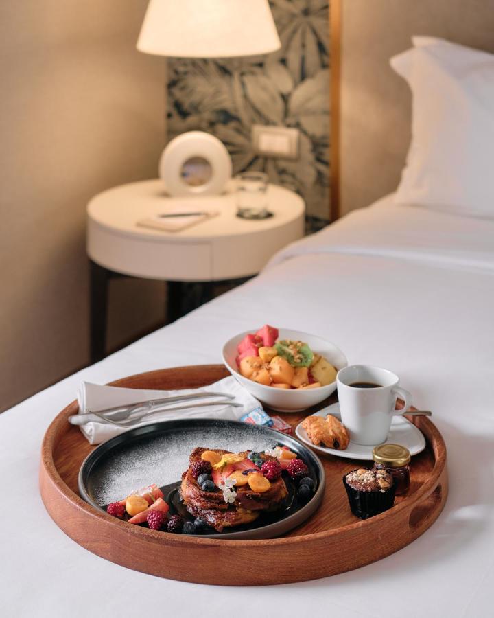 9 Unique Boutique Hotels in Lima 14 A wooden tray on a neatly made hotel bed in one of Lima Peru’s boutique hotels holds French toast with berries, fresh fruit, a croissant, muffin, butter, jam, and coffee. A lamp and clock rest on the bedside table in the background.
