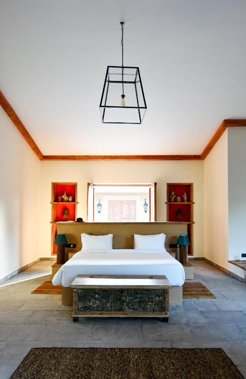 12 BEST Boutique Hotels in Jaipur 28 Modern bedroom with a double bed, white bedding, two side tables with lamps, red shelves displaying decor, a large window behind the bed, and a geometric pendant light—evoking the elegance of boutique hotels in Jaipur.