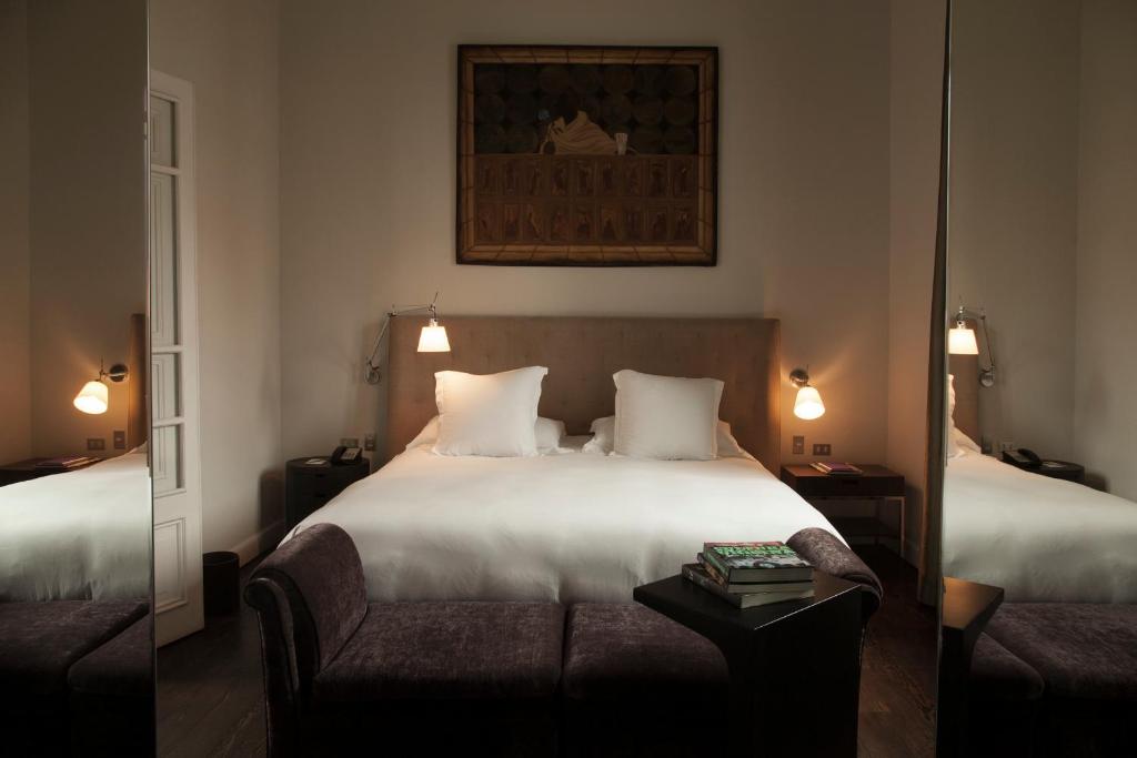 9 Unique Boutique Hotels in Lima 27 A neatly made bed with white linens sits against a beige headboard in a cozy, softly lit hotel room—an inviting scene often found in boutique hotels in Lima. Two bedside tables with lamps and a painting above complete the warm ambience.