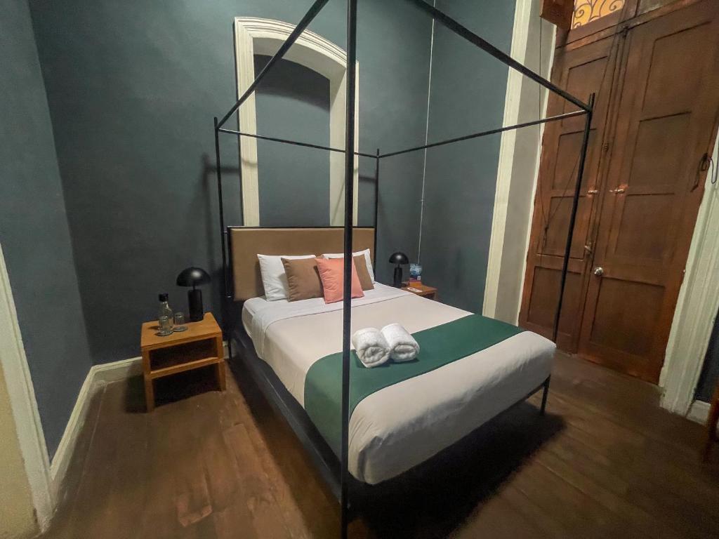 9 Unique Boutique Hotels in Lima 38 A cozy bedroom in the style of boutique hotels in Lima, featuring a four-poster bed with green and white bedding, three pillows, two rolled towels, wooden nightstands with lamps and water bottles, dark walls, wooden floors, and a large wardrobe.
