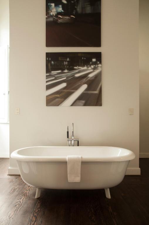 9 Unique Boutique Hotels in Lima 30 A modern white freestanding bathtub with a folded white towel draped over the edge evokes the luxurious feel of boutique hotels in Lima, set against a white wall with cityscape art above and a dark wooden floor below.