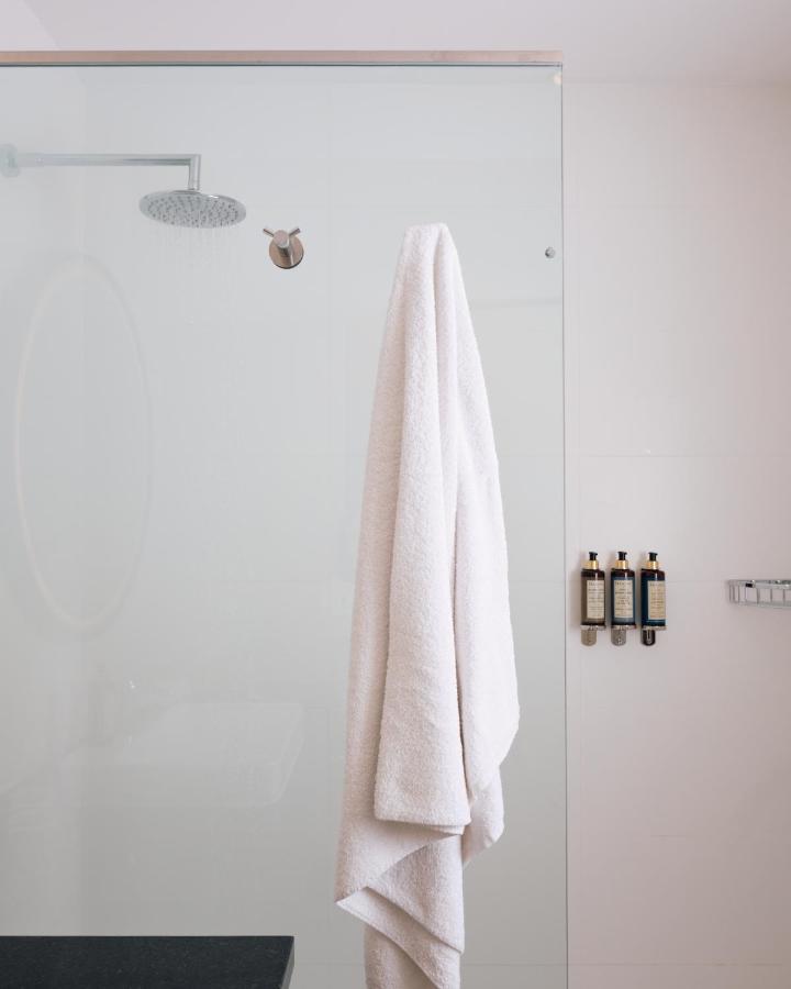 9 Unique Boutique Hotels in Lima 15 A white bathrobe hangs on a hook on a glass shower wall, with a rainfall showerhead and three bottles of toiletries nearby—evoking the luxury found in boutique hotels in Lima, Peru.