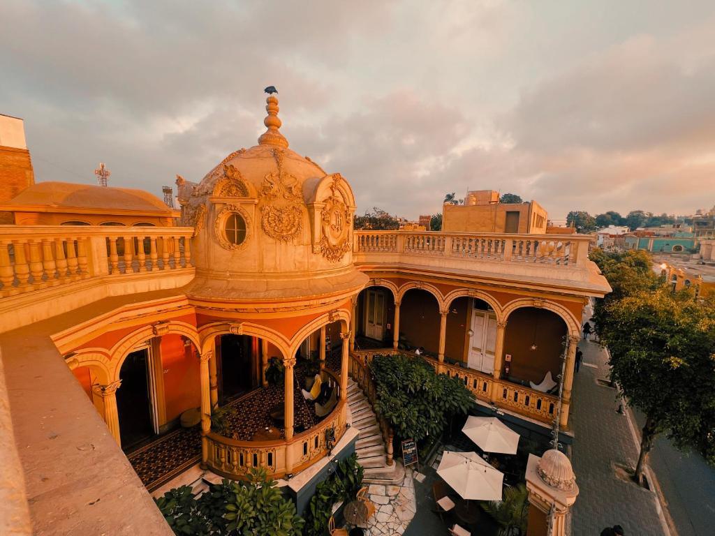 9 Unique Boutique Hotels in Lima 35 A grand, ornate building with a domed roof and columns, bathed in warm sunset light. The courtyard below, reminiscent of boutique hotels in Lima, features greenery, white umbrellas, tiled floors, and a staircase to the upper level.