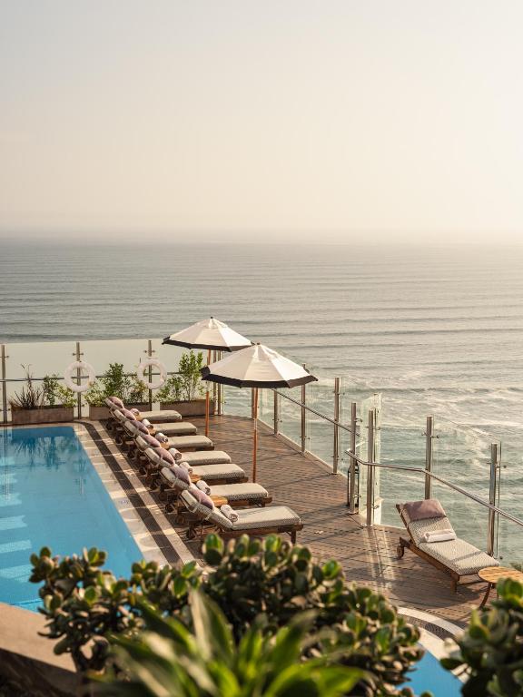 9 Unique Boutique Hotels in Lima 31 A pool with lounge chairs and umbrellas on a rooftop overlooking the ocean, perfect for relaxing at one of the boutique hotels in Lima.