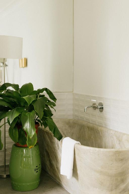 9 Unique Boutique Hotels in Lima 26 A beige stone bathtub with a white towel draped over the side sits next to a large green potted plant and a floor lamp in a bright, modern bathroom with white tiled walls, reminiscent of boutique hotels in Lima.