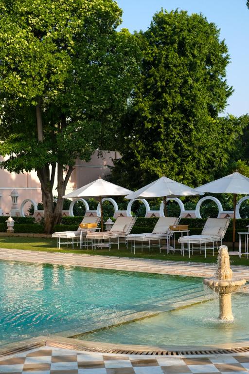 12 BEST Boutique Hotels in Jaipur 15 A serene outdoor pool area at one of the boutique hotels in Jaipur, featuring white lounge chairs under circular canopies, a small fountain, and lush green trees and bushes surrounding the peaceful space.