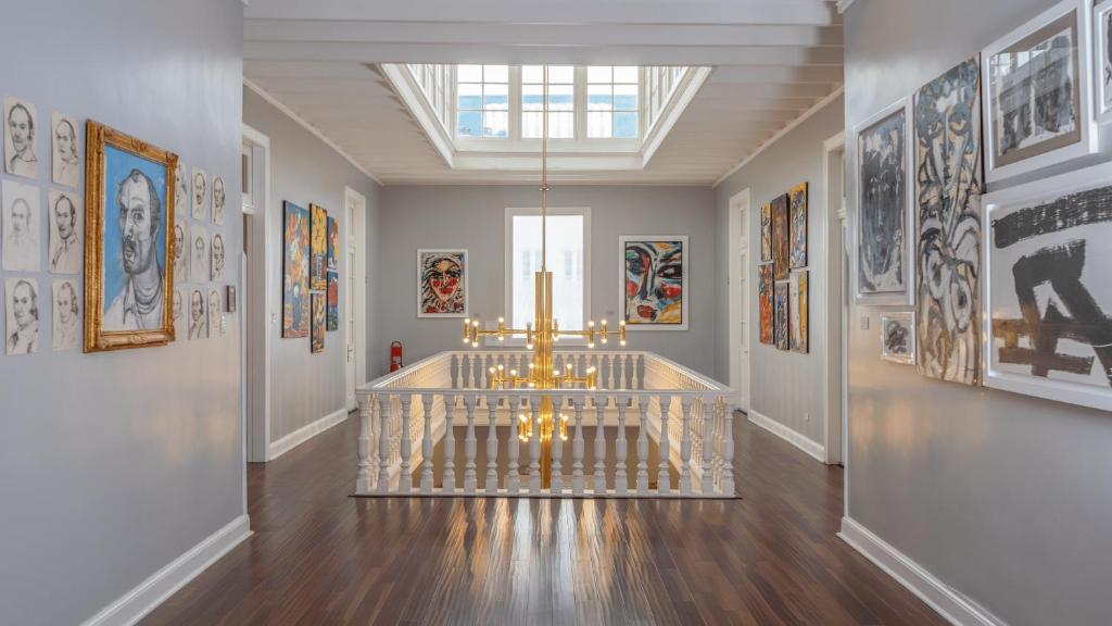 9 Unique Boutique Hotels in Lima 40 A bright, modern art gallery with polished wood floors, gray walls, a central white banister, and a gold chandelier, reminiscent of the vibrant aesthetics found in boutique hotels in Lima, with colorful paintings and portraits displayed along both walls.