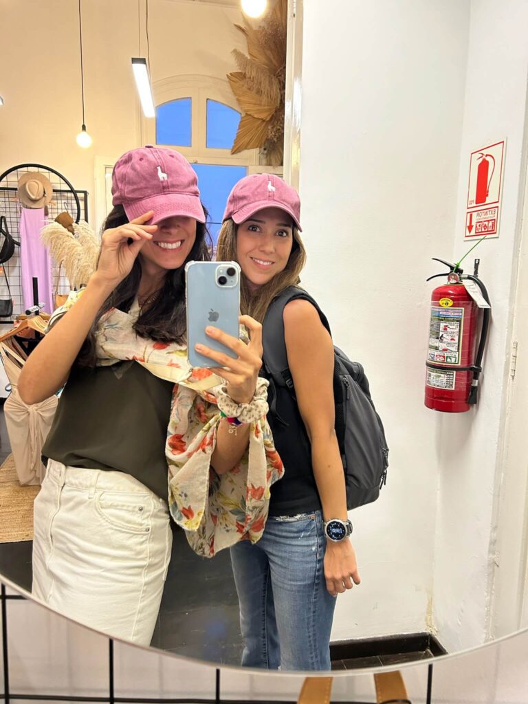 9 Unique Boutique Hotels in Lima 49 Two women pose and smile in front of a mirror at one of the boutique hotels in Lima, both wearing pink caps. One holds a phone, partially covering her face. They are casually dressed; a fire extinguisher and a large window appear in the background.
