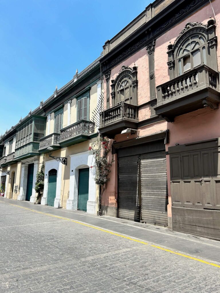 9 Unique Boutique Hotels in Lima 50 A street view of historic buildings with ornate wooden balconies, colorful facades in green and pink—reminiscent of boutique hotels in Lima—and closed doors and shutters under a clear blue sky.