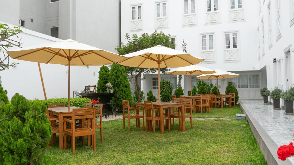 9 Unique Boutique Hotels in Lima 41 Outdoor courtyard with wooden tables and chairs under large beige umbrellas, surrounded by green shrubs and the white walls of a boutique hotel in Lima, creating a calm and inviting atmosphere.
