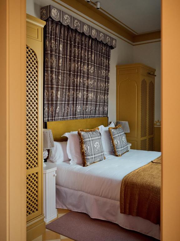 Elegant bedroom with a mustard yellow theme, similar to chic boutique hotels in Seville, featuring a double bed with white linens, patterned throw pillows, a matching blanket, ornate headboard, decorative curtains, and two yellow wardrobes.