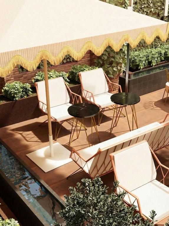 Outdoor patio with white and gold chairs around black tables, set beside a narrow water feature. A canopy with yellow fringe shades part of the area, and green plants decorate the space. The scene is sunny and inviting—reminiscent of the stylish charm found at boutique hotels in Seville.