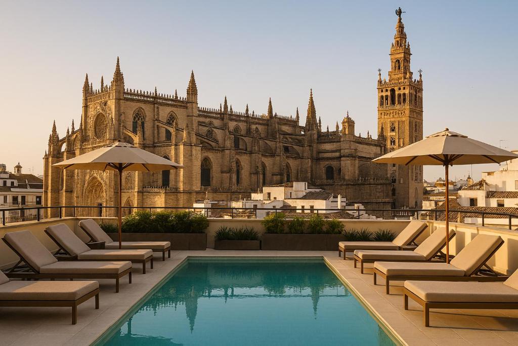 A rooftop pool with lounge chairs and umbrellas overlooks the Seville Cathedral and Giralda tower under a clear sky at sunset, capturing the exclusive atmosphere found in some of the finest boutique hotels in Seville.
