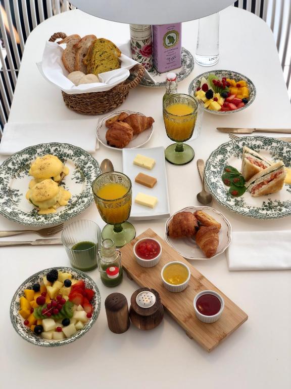 Reminiscent of the refined breakfasts served at boutique hotels in Seville, this elegant spread features eggs benedict, croissants, sandwiches, fruit bowls, juice, jams, butter, a bread basket, and condiments—all beautifully arranged on a white table with vintage-patterned plates and glassware.