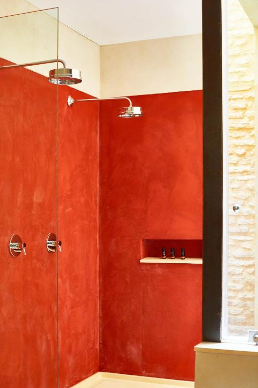 Modern shower with red textured walls, a glass partition, two showerheads, built-in shelf, and black fixtures, next to a window with light stone texture—evoking the luxurious style often found in boutique hotels in Seville.