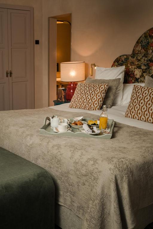 A neatly made bed with patterned pillows, a floral headboard, and a breakfast tray holding tea, juice, and food—this inviting scene captures the intimate charm often found in boutique hotels in Seville. A lamp and nightstand are placed thoughtfully beside the bed.